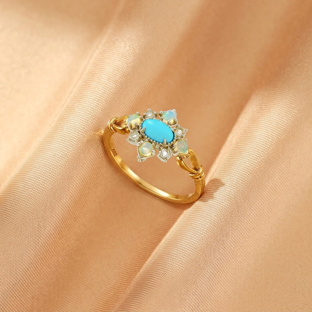 Bague en argent plaqué or 14K sertie d'une turquoise ovale centrale, entourée d'opales et de diamants scintillants, posée sur un tissu satiné couleur pêche.