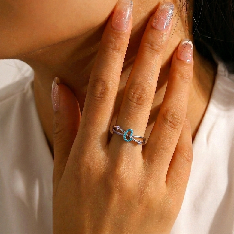 Bague en argent avec un motif ovale turquoise et des accents violets, portée à l'annulaire d'une main aux ongles vernis.