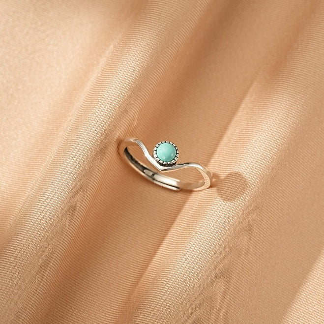 Bague en argent avec une petite turquoise ronde sertie sur un design ondulé inspiré des vagues.