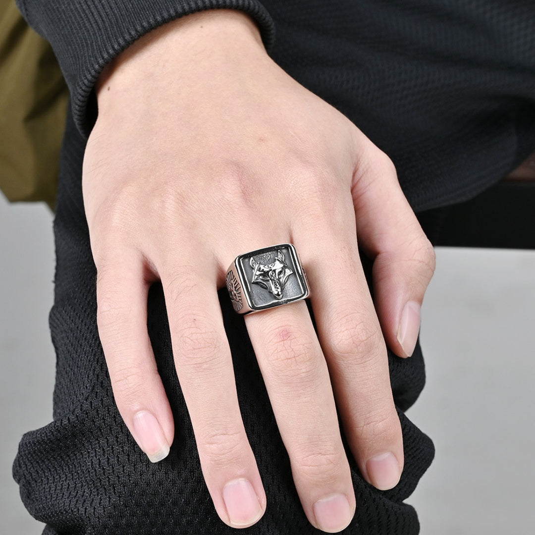 Bague Viking unisexe "Regard Sauvage" ornée d'une tête de loup stylisée sur un plateau carré, fabriquée en argent vieilli et portée à l'annulaire d'une main masculine.