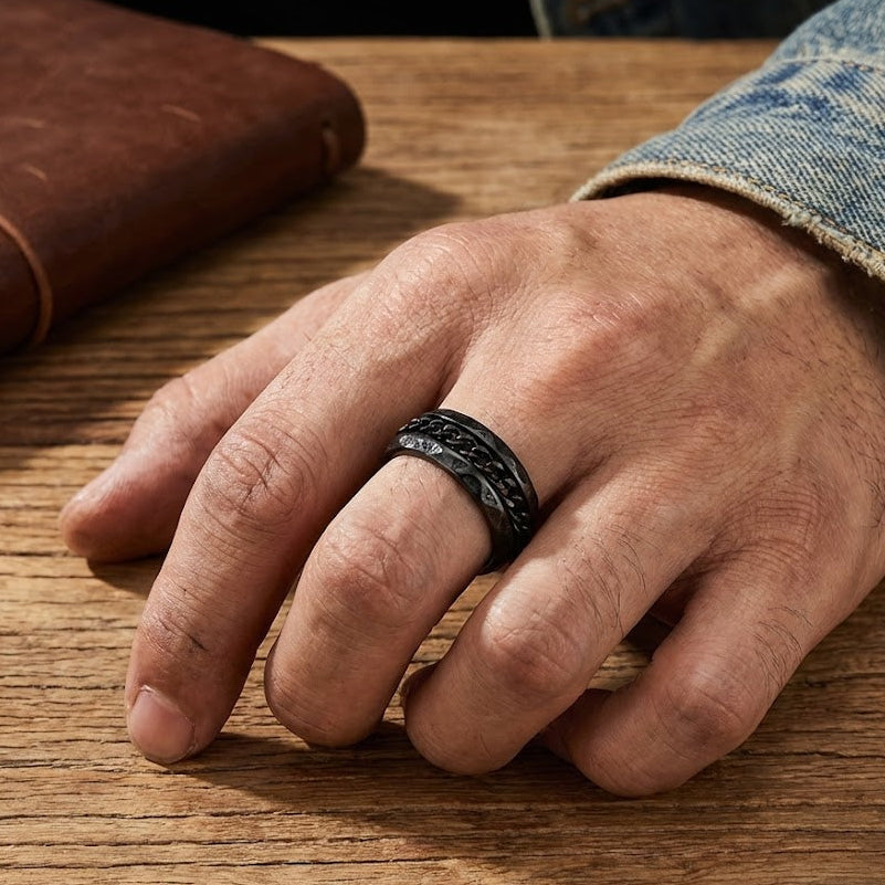 Bague Viking Souveraineté Noire pour homme, en acier noir, avec une texture de chaîne au centre et un bord texturé, portée à l'annulaire.