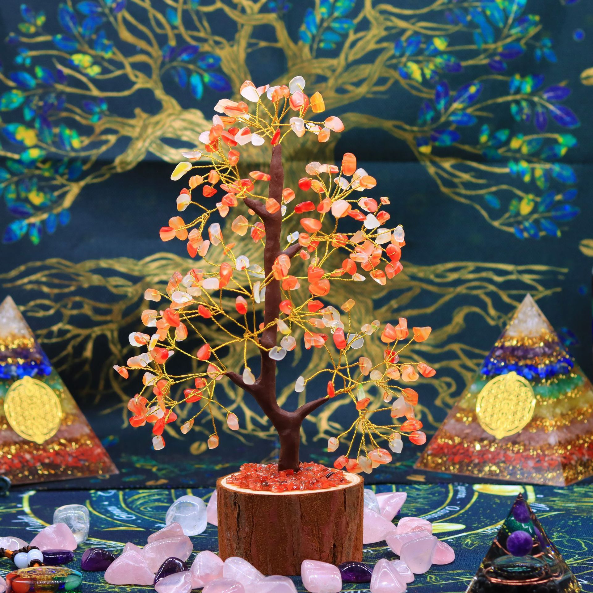Arbre de Vie en pierres de 7 chakras multicolores, posé sur un socle en bois, entouré de pierres roses et de pyramides spirituelles, sur un fond orné d'un Arbre de Vie bleu et doré.