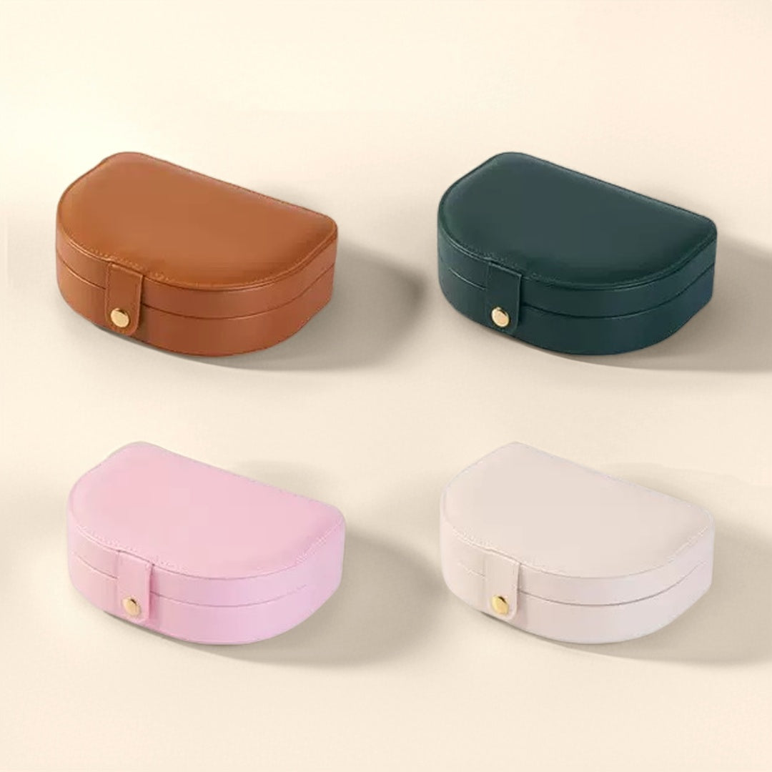 Quatre boîtes à bijoux en forme de demi-lune, disponibles en marron, vert forêt, rose et blanc cassé, chacune avec une fermeture dorée.