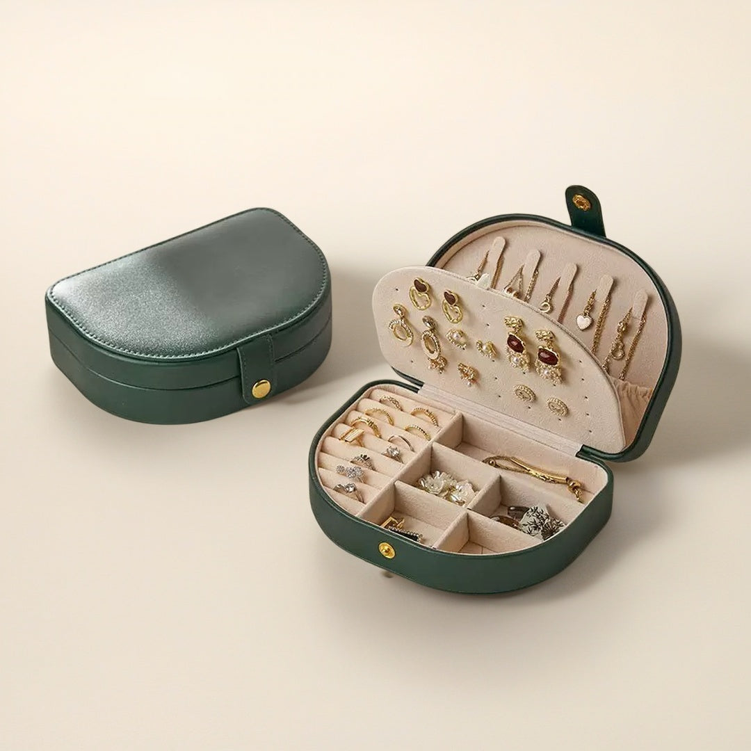 Boîte à bijoux en cuir vert foncé ouverte, remplie de bijoux dorés et argentés, y compris des bagues, des boucles d'oreilles et des colliers. Une boîte fermée est placée sur le côté gauche.