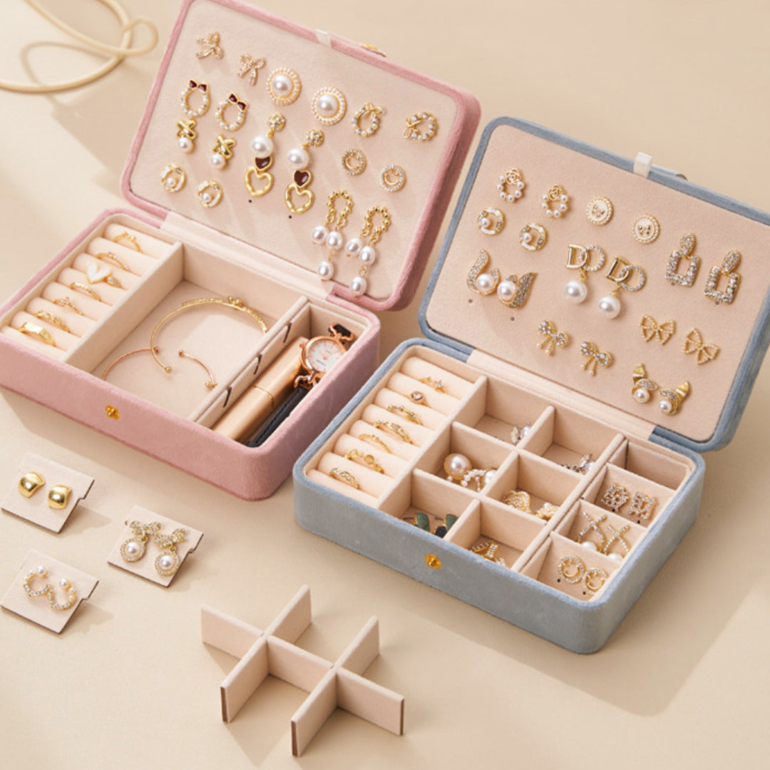 Deux boîtes à bijoux en velours ouvertes, une rose et une bleue, remplies de divers bijoux dorés et nacrés, y compris des boucles d'oreilles, des bagues et un bracelet.