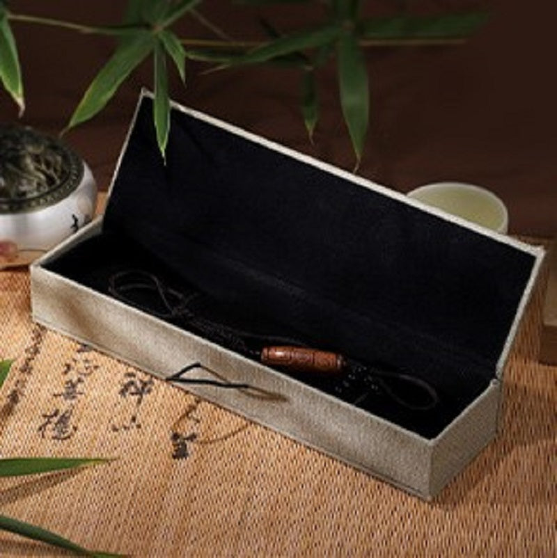 Boîte cadeau zen en lin beige ouverte, avec un pendentif en bois à l'intérieur, posée sur un tapis de paille.