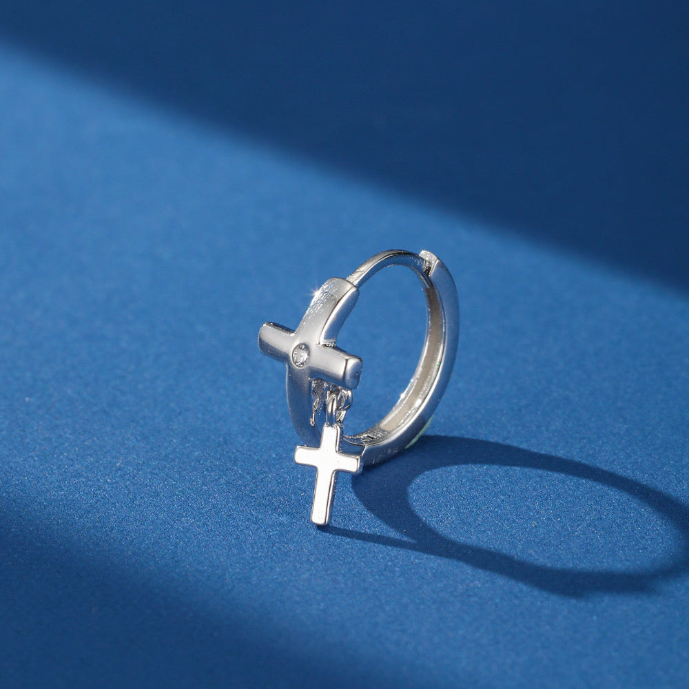 Boucle d'oreille homme en argent avec un pendentif croix double, sur fond bleu avec une ombre.