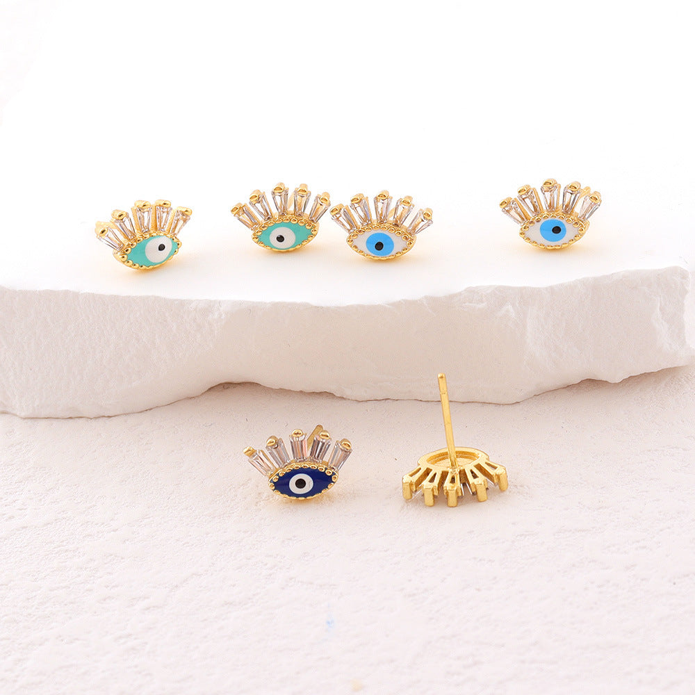 Boucles d'oreilles dorées en forme d'œil bleu avec des zircons cubiques scintillants sur fond blanc