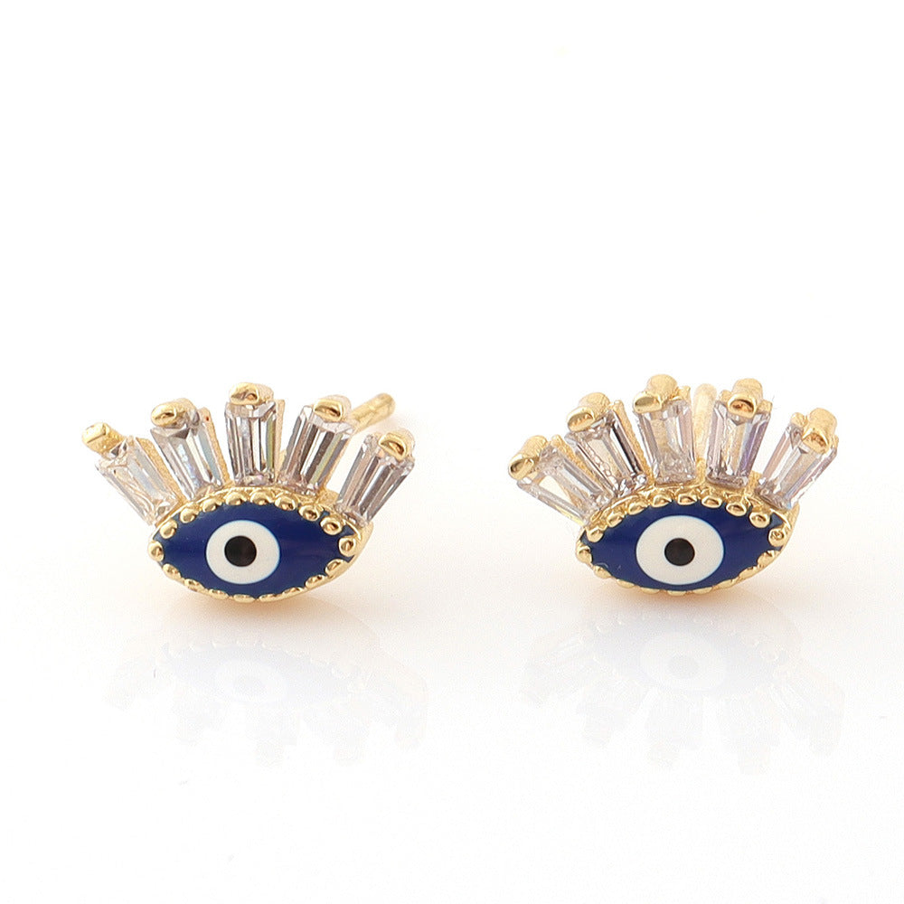 Une paire de boucles d'oreilles en forme d'œil bleu avec des cristaux blancs scintillants et une monture dorée, style mauvais œil.