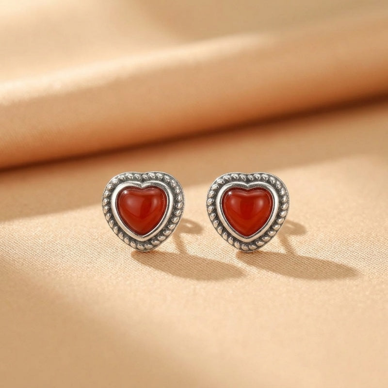 Boucles d'oreilles en argent ornées d'une pierre d'agate rouge en forme de cœur, avec une bordure texturée.