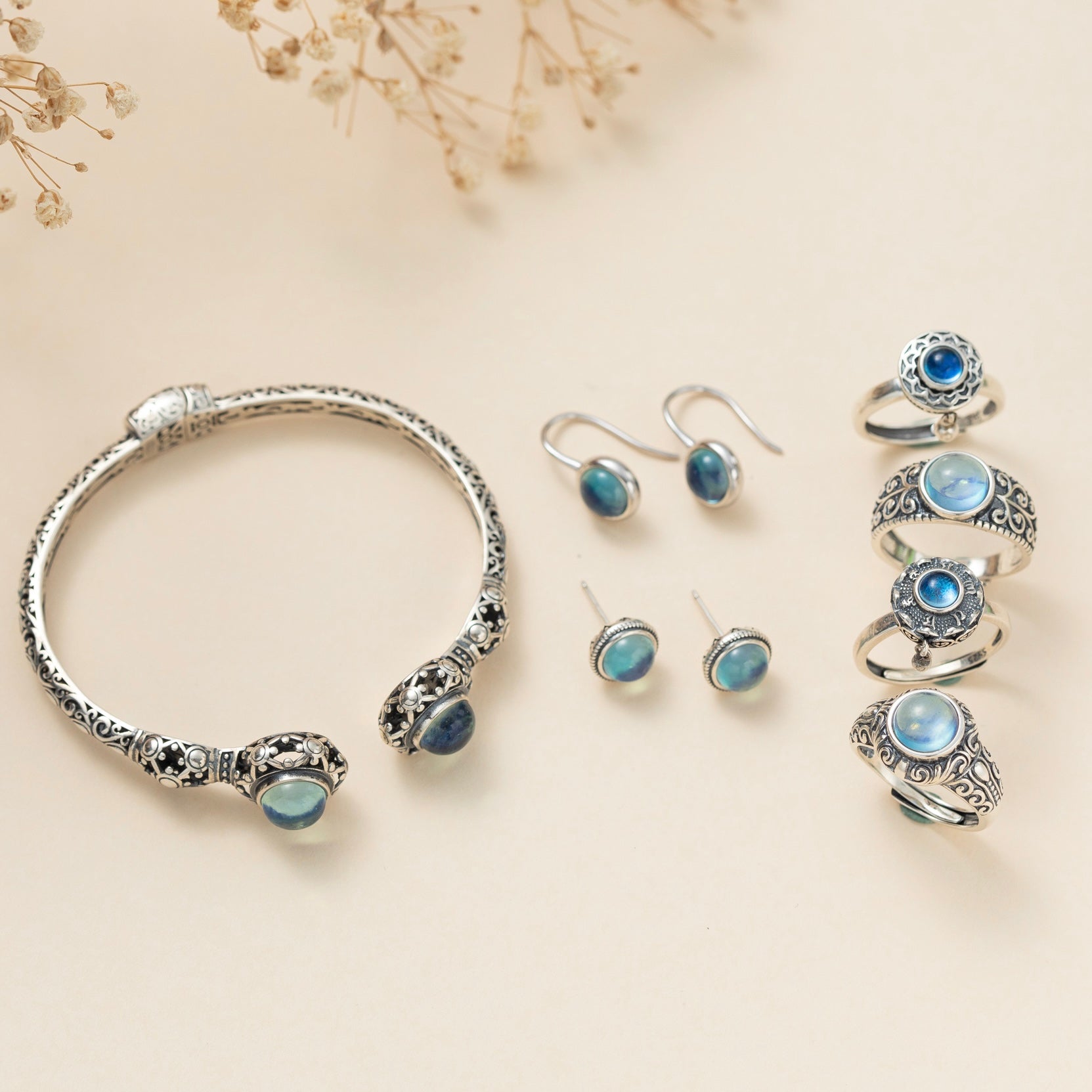 Ensemble de bijoux en argent avec des pierres d'aigue-marine bleues, comprenant un bracelet ouvert, des boucles d'oreilles pendantes, des clous d'oreilles et plusieurs bagues ornées.