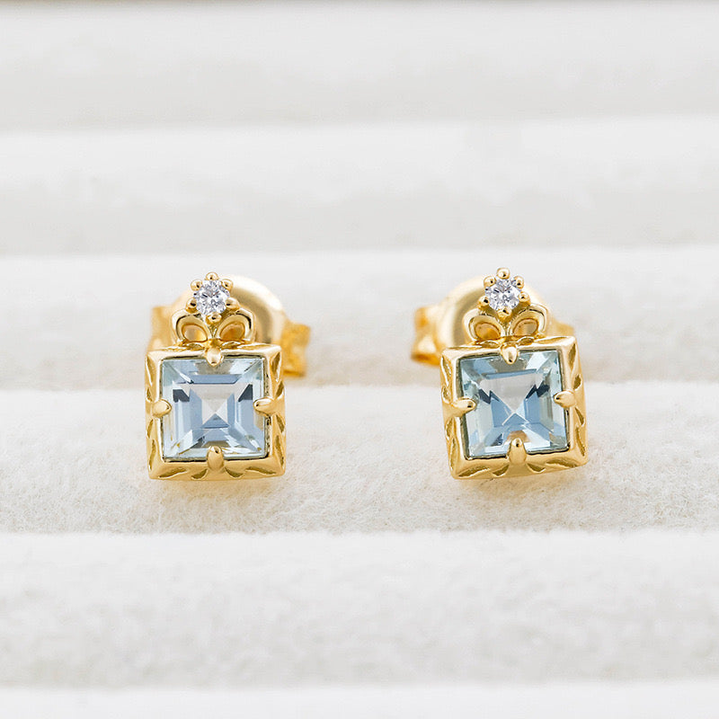 Paire de boucles d'oreilles en plaqué or ornées d'aigues-marines bleues carrées et d'un petit diamant serti en forme de couronne.