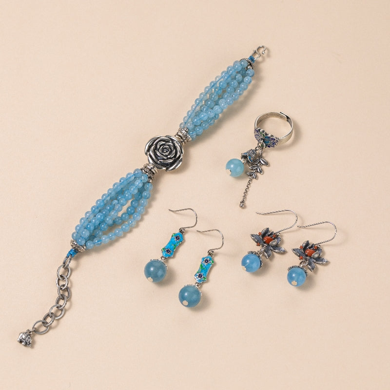Ensemble de bijoux en argent et aigue-marine comprenant un bracelet à plusieurs rangs orné d'une rose, une bague à pendentif floral et deux paires de boucles d'oreilles assorties.