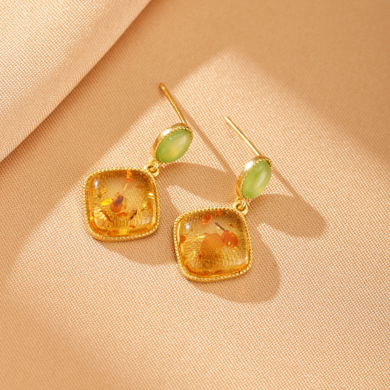 Boucles d'oreilles pendantes Feu Doré en argent plaqué or avec pierre d'ambre carrée et jade vert ovale sur fond beige