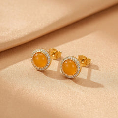 Paire de boucles d'oreilles en ambre et argent plaqué or, serties de petits zircons brillants, sur un fond en tissu beige.