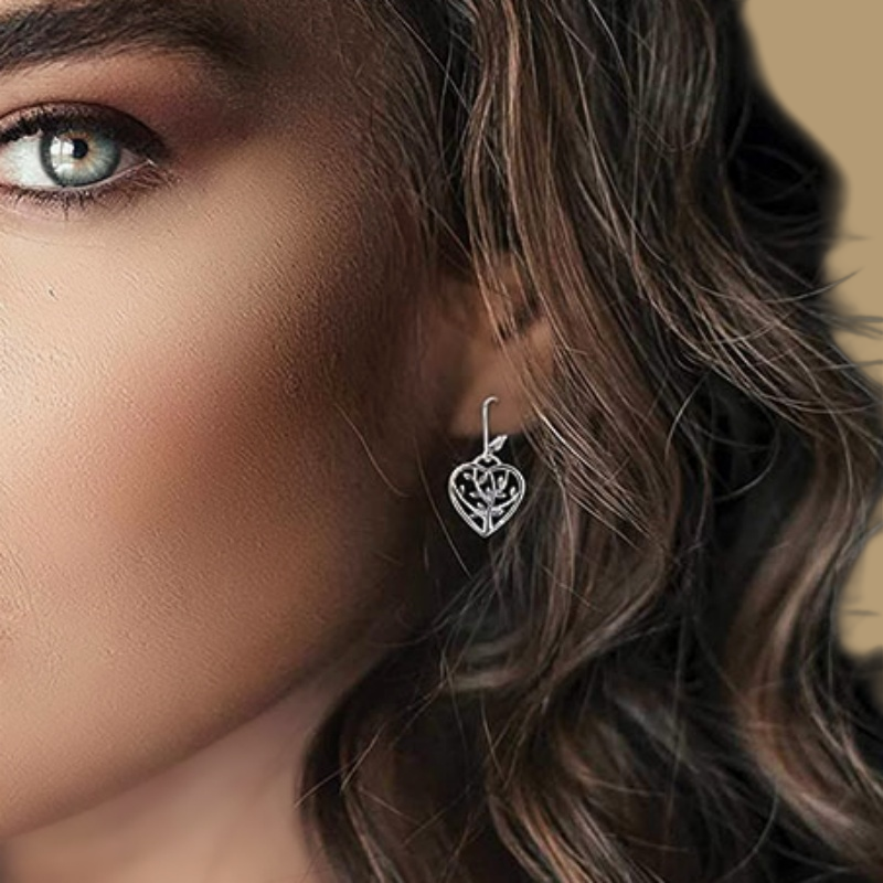 Boucles d'oreilles en forme de cœur ajouré avec un motif d'arbre de vie, en argent 925, portées par une femme.