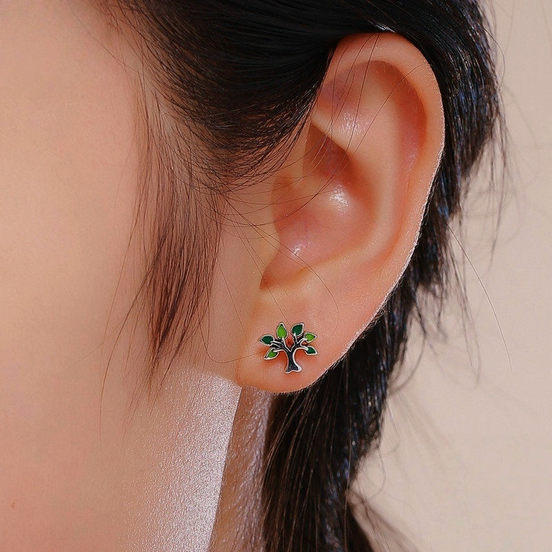 Boucle d'oreille en argent représentant un arbre de vie avec des feuilles vertes et rouges, portée à l'oreille.