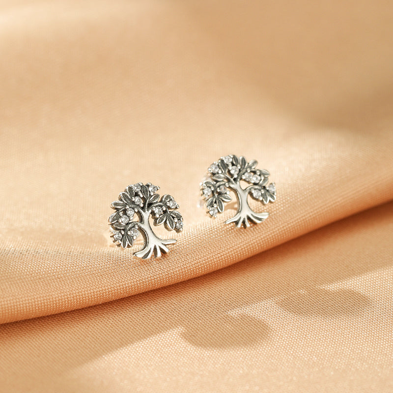 Paire de boucles d'oreilles en argent 925 représentant un arbre de vie orné de petites pierres scintillantes, sur un fond soyeux.
