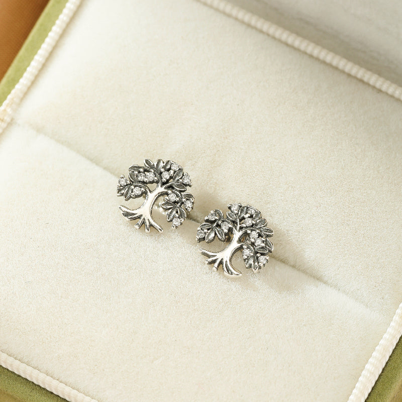 Boucles d'oreilles Arbre de Vie en argent 925 serties de petites pierres scintillantes, présentées dans une boîte à bijoux verte.