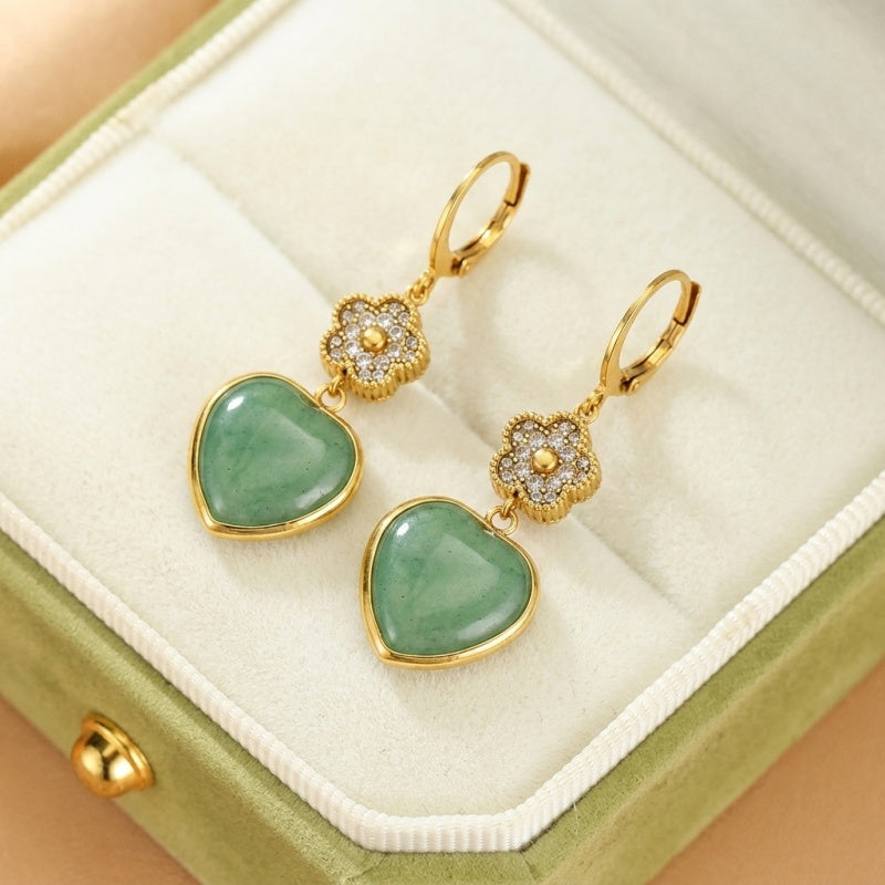 Boucles d'oreilles pendantes en aventurine verte en forme de cœur, ornées de petites fleurs pavées de cristaux et d'une finition dorée, présentées dans une boîte à bijoux verte.