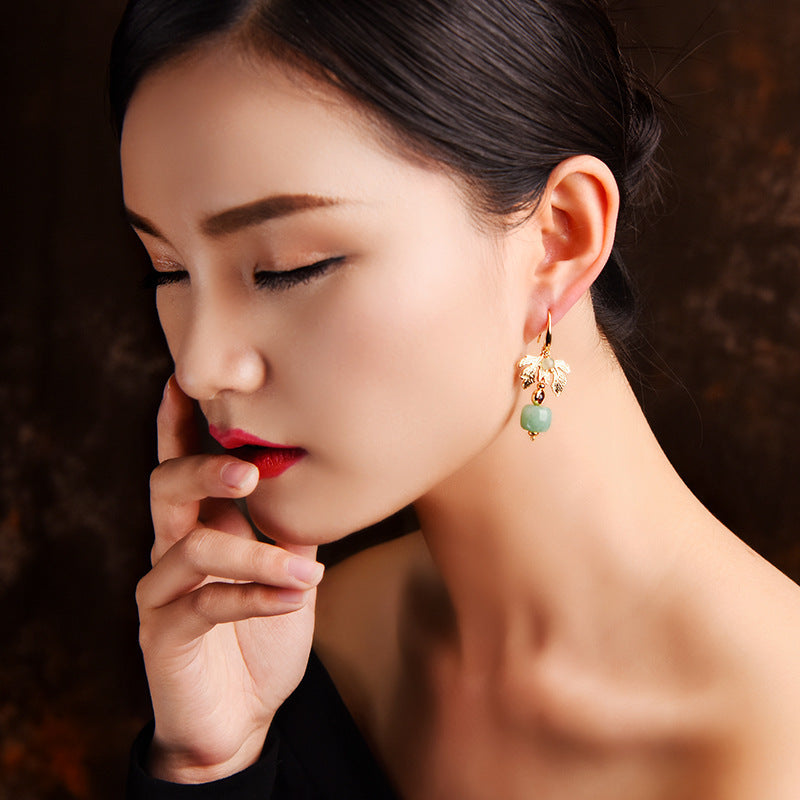 Boucles d'oreilles plaquées or avec une petite pierre d'aventurine verte en forme de cœur suspendue à une feuille dorée.
