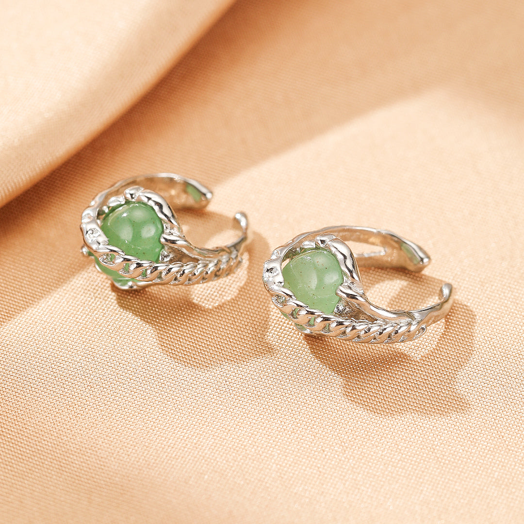 Deux boucles d'oreilles argentées ornées de perles rondes vertes en aventurine, posées sur un tissu beige.