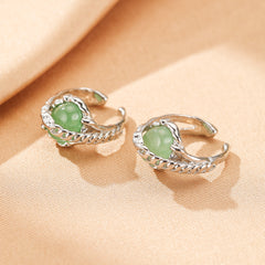 Deux boucles d'oreilles argentées ornées de perles rondes vertes en aventurine, posées sur un tissu beige.