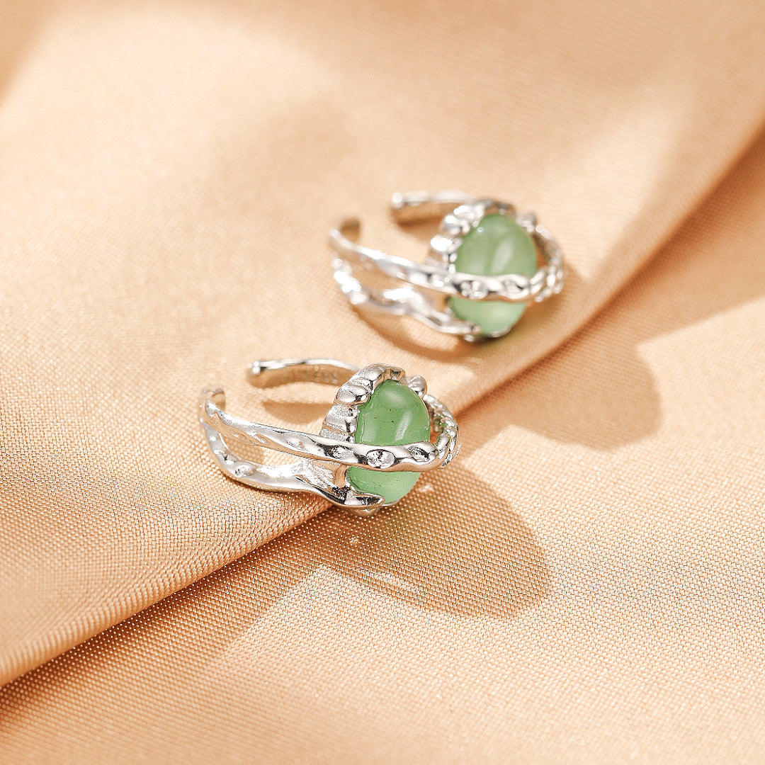 Deux boucles d'oreilles en argent ornées de pierres vertes ovales, montées sur un fond beige satiné.