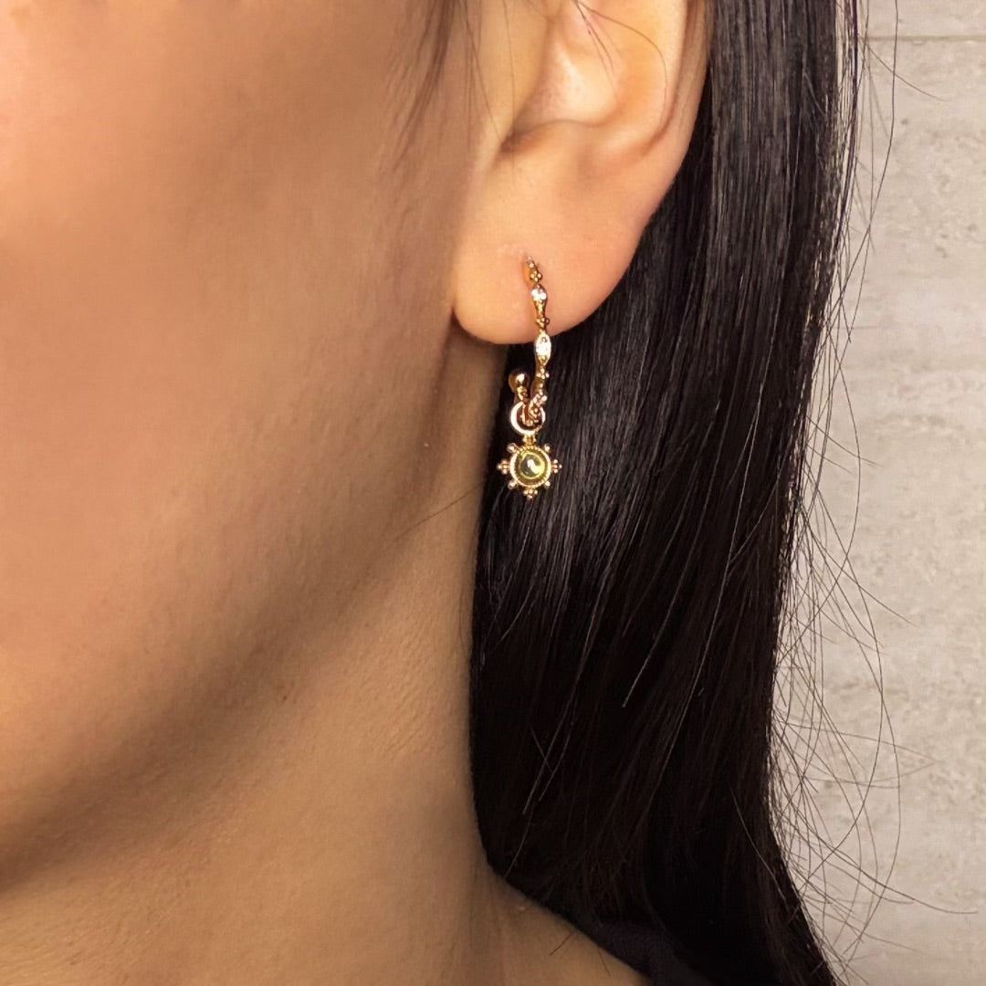 Boucle d'oreille créole plaquée or avec une pierre péridot ronde au centre et des petits cristaux sur la chaîne.