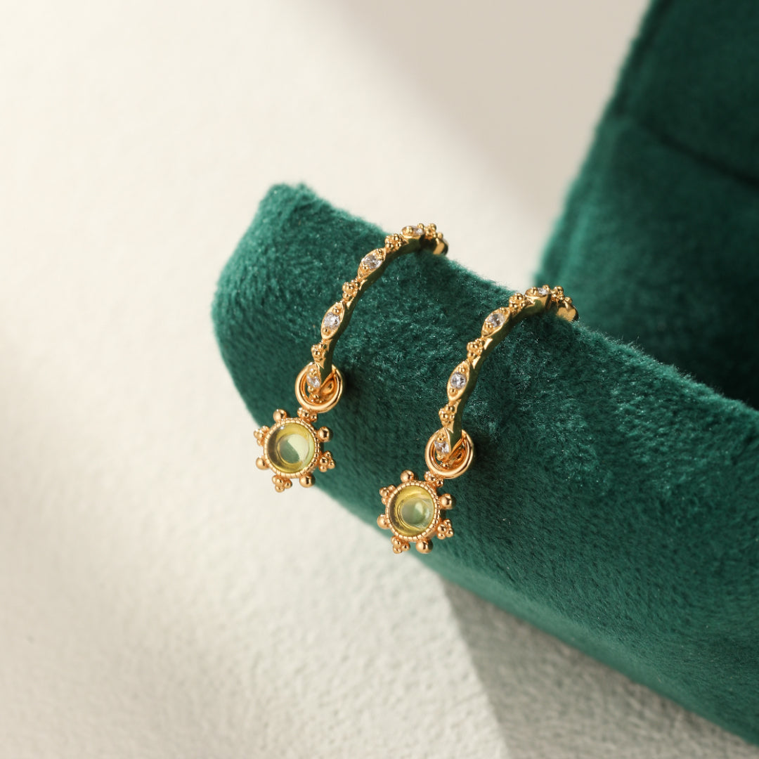 Boucles d'oreilles créoles plaqué or avec pendentif soleil en péridot et zirconium, serti de petites billes dorées.