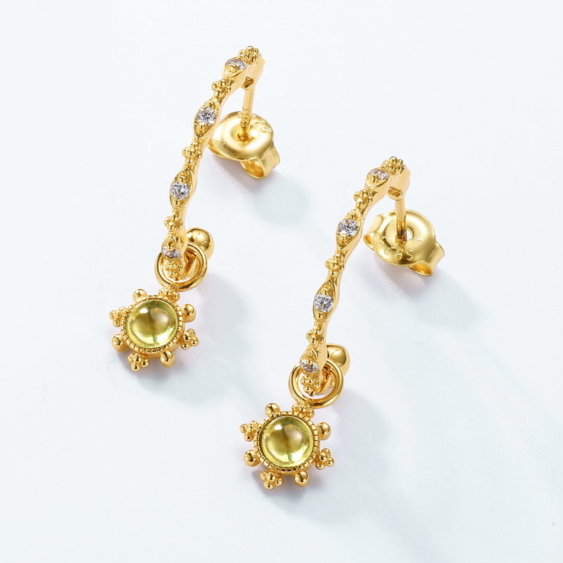 Boucles d'oreilles créoles pendantes plaquées or avec des péridots ronds sertis en soleil et des petites pierres scintillantes.