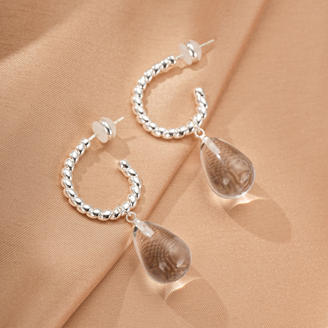 Boucles d’oreilles créoles argentées torsadées avec pendentifs en forme de goutte de cristal de roche fumé.