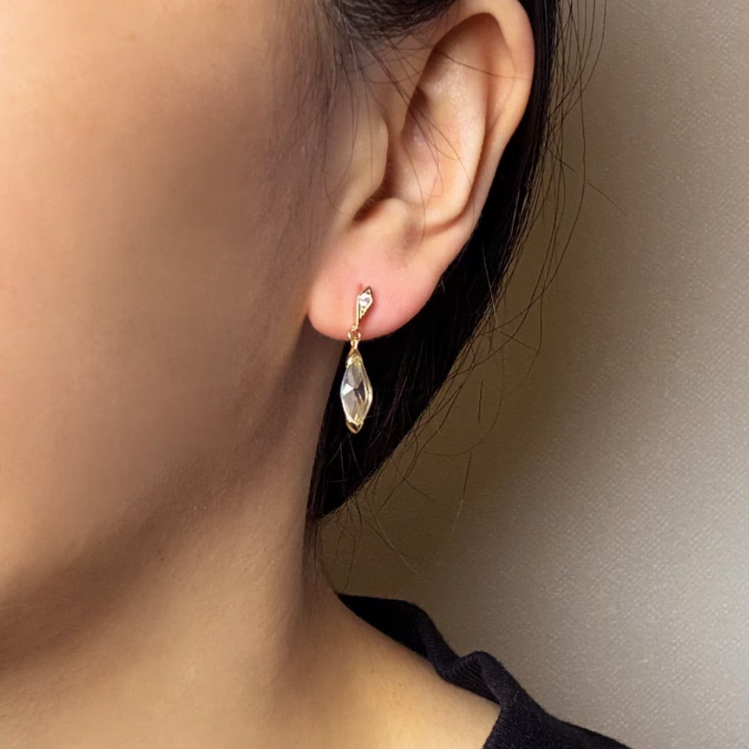 Boucle d'oreille pendant en cristal de roche clair, avec une petite pierre cubique à l'attache, sur un lobe d'oreille.