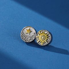 Paire de boucles d'oreilles homme Duo Cosmique avec un motif lune et étoile sur une boucle et un soleil stylisé sur l'autre, sur fond bleu.