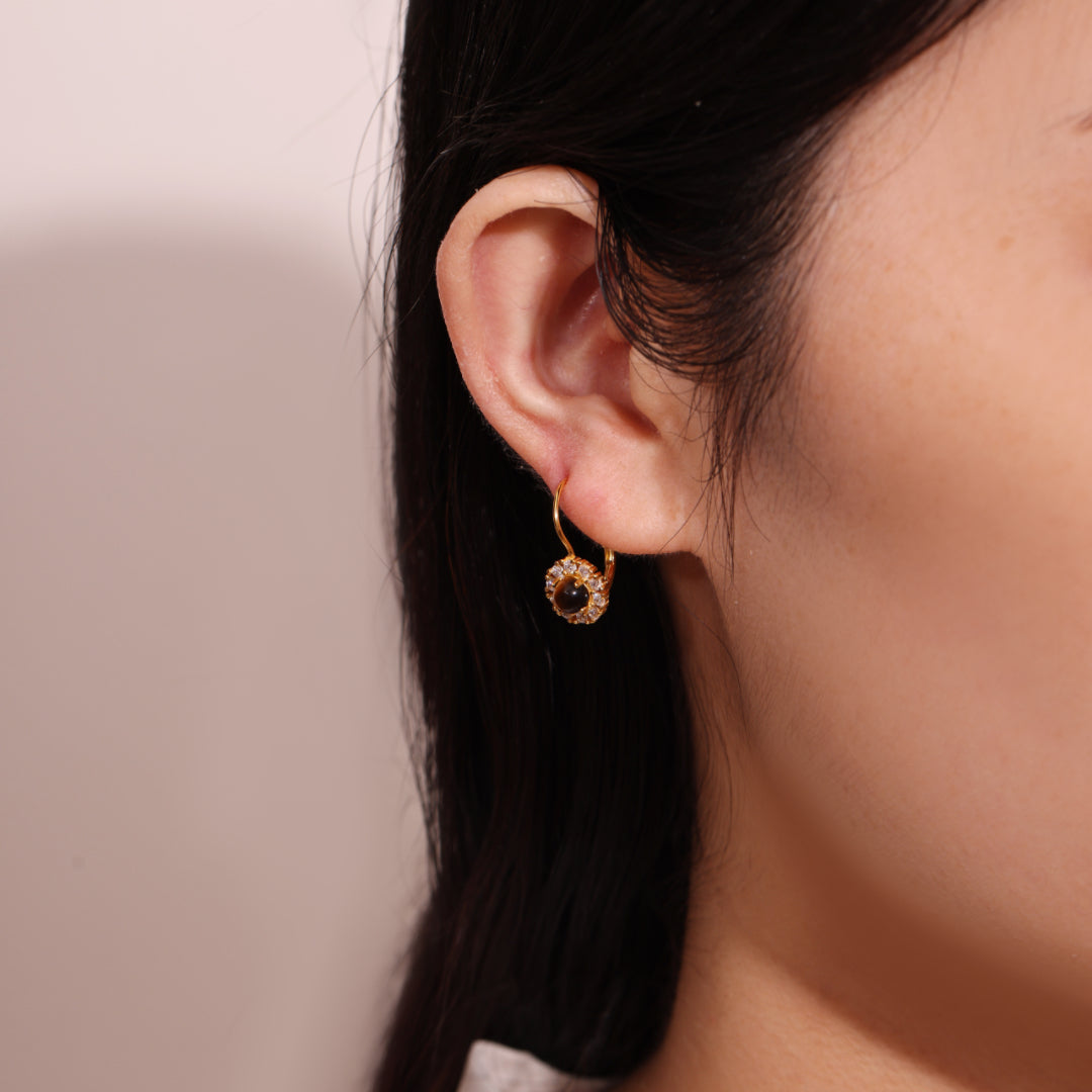 Boucle d'oreille plaqué or avec une pierre centrale foncée entourée de zircons et une bélière ornée de zircons