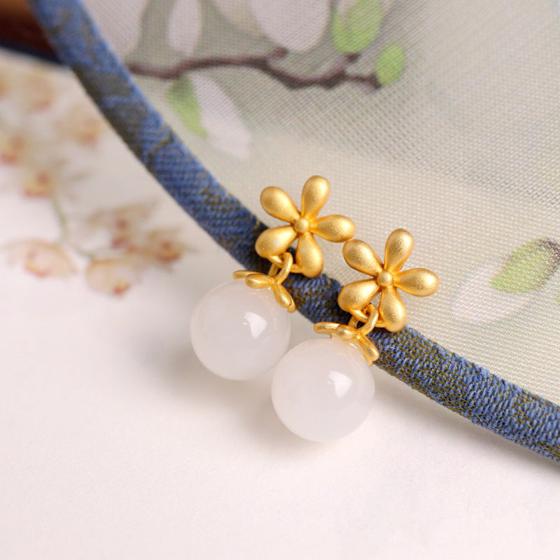 Boucles d'oreilles en argent plaqué or avec des perles de jade blanc et des motifs de fleurs dorées.