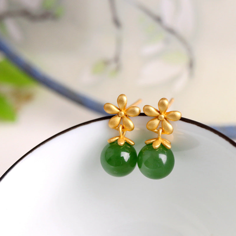 Boucles d’oreilles élégantes en jade vert avec des motifs de fleurs en argent plaqué or, présentées sur une soucoupe blanche.