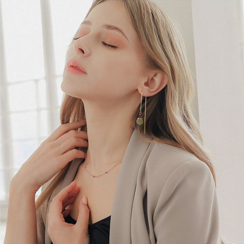Boucles d’oreilles pendantes en argent plaqué or avec une agate verte et une perle rouge, portées par une femme blonde.