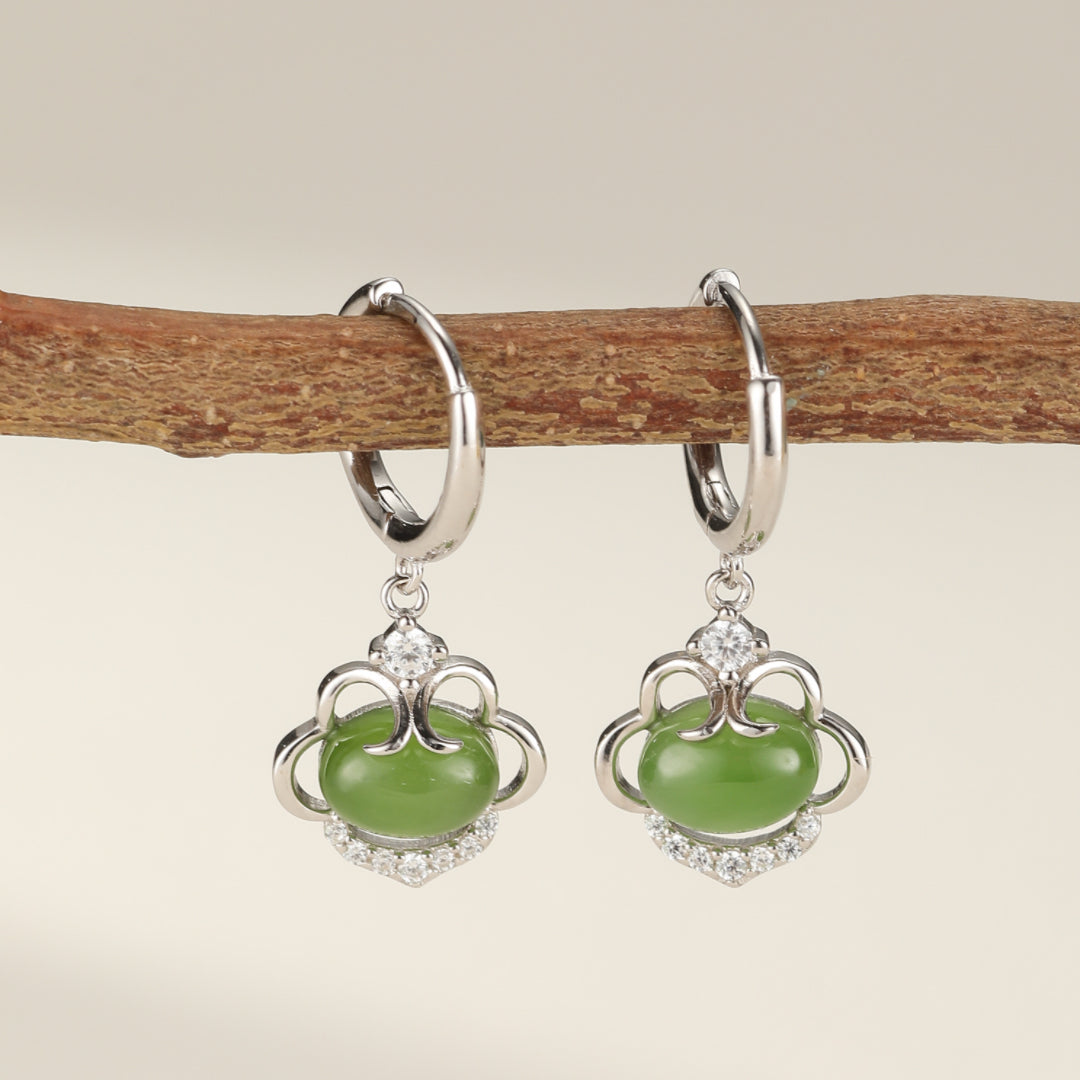 Boucles d'oreilles argentées ornées de jade vert et de cristaux scintillants, suspendues à une branche.