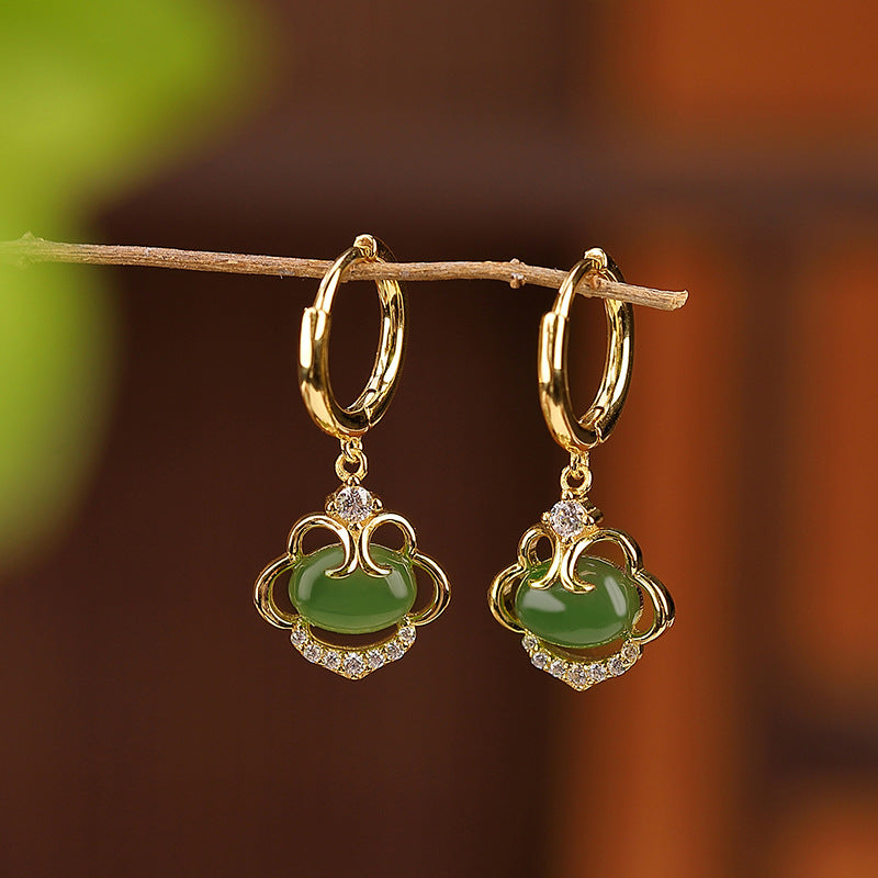 Paire de boucles d'oreilles pendantes en argent doré serties d'une pierre de jade verte ovale et de petits zircons scintillants, suspendues à une branche.