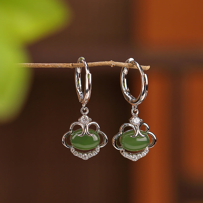 Boucles d'oreilles en argent avec une pierre de jade verte et des détails en zircon cubique, suspendues à une branche.