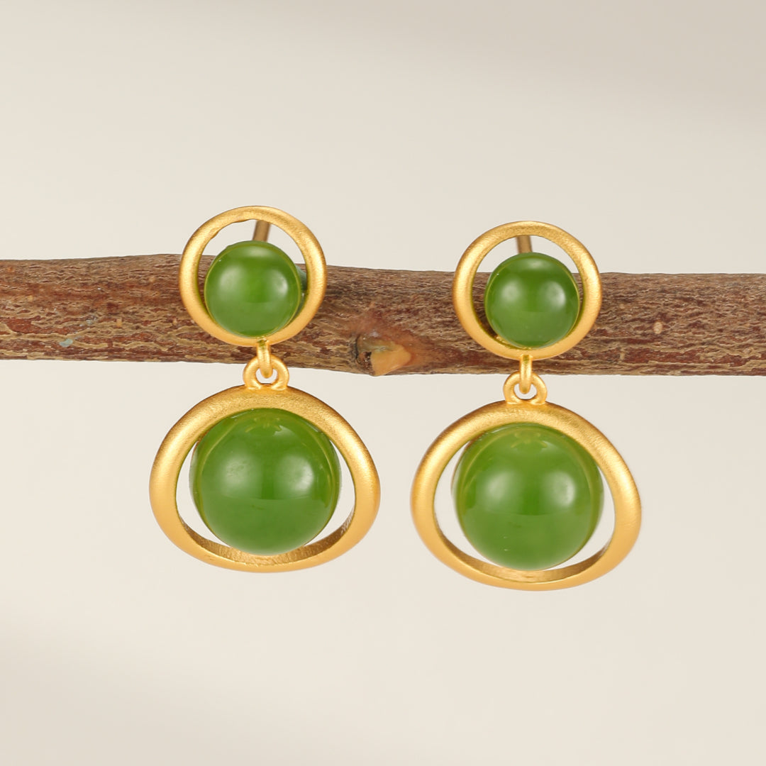 Boucles d'oreilles pendantes en argent plaqué or avec deux perles rondes de jade vert, montées sur une branche.