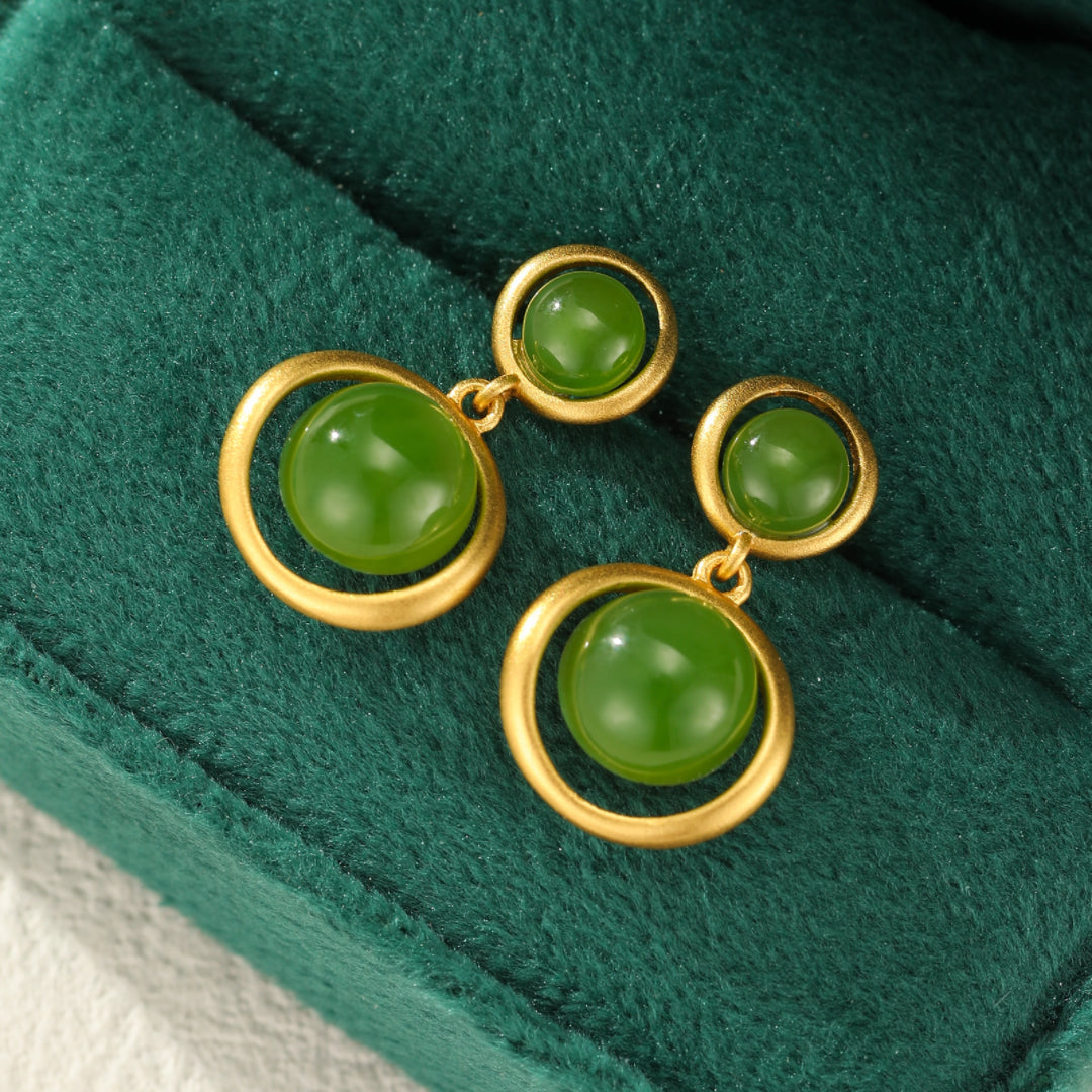 Boucles d'oreilles pendantes en jade vert vif et argent plaqué or, avec un design double anneau, présentées sur un écrin en velours vert.