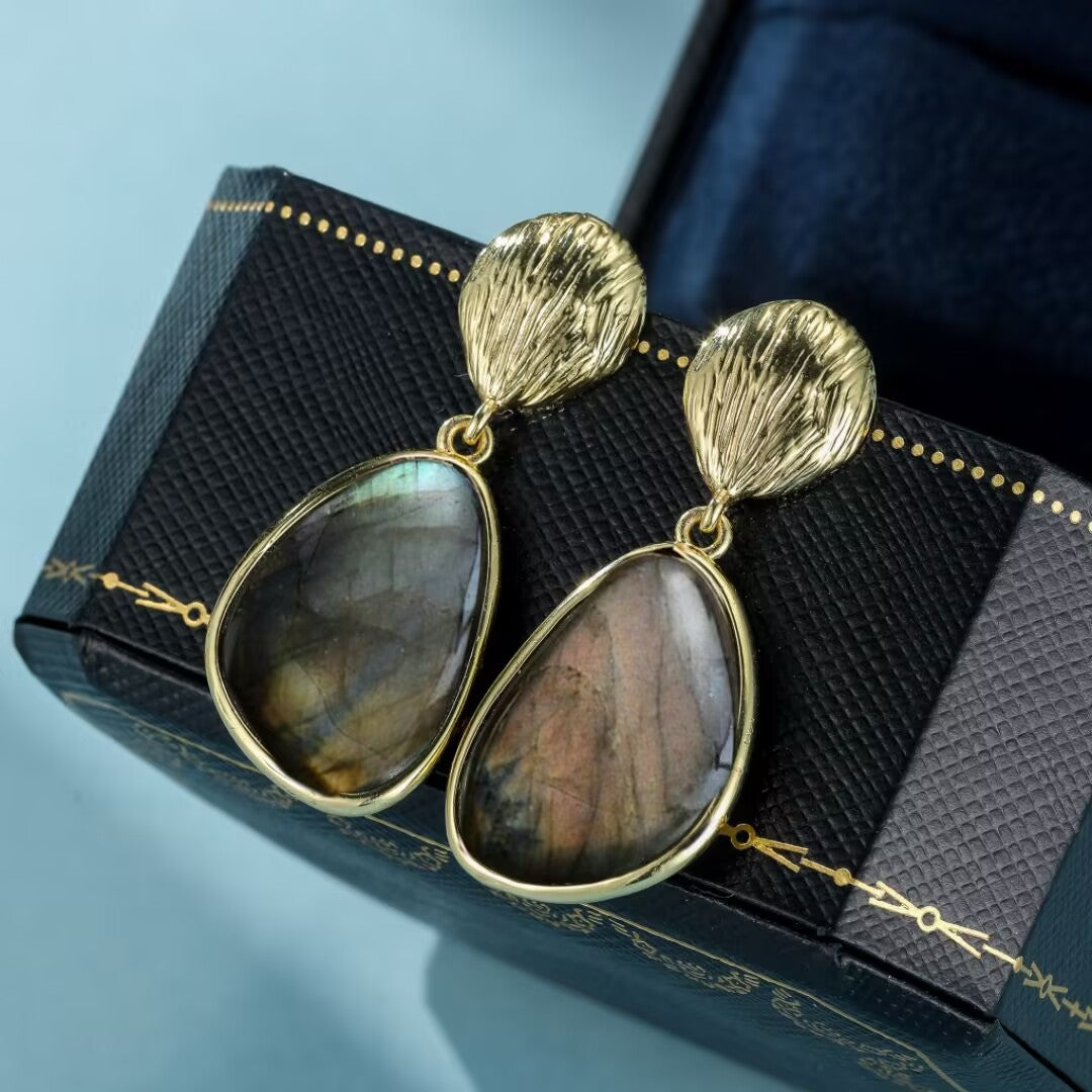 Boucles d'oreilles pendantes en argent plaqué or avec pierres de labradorite aux reflets bleus et roses, présentées dans une boîte à bijoux.