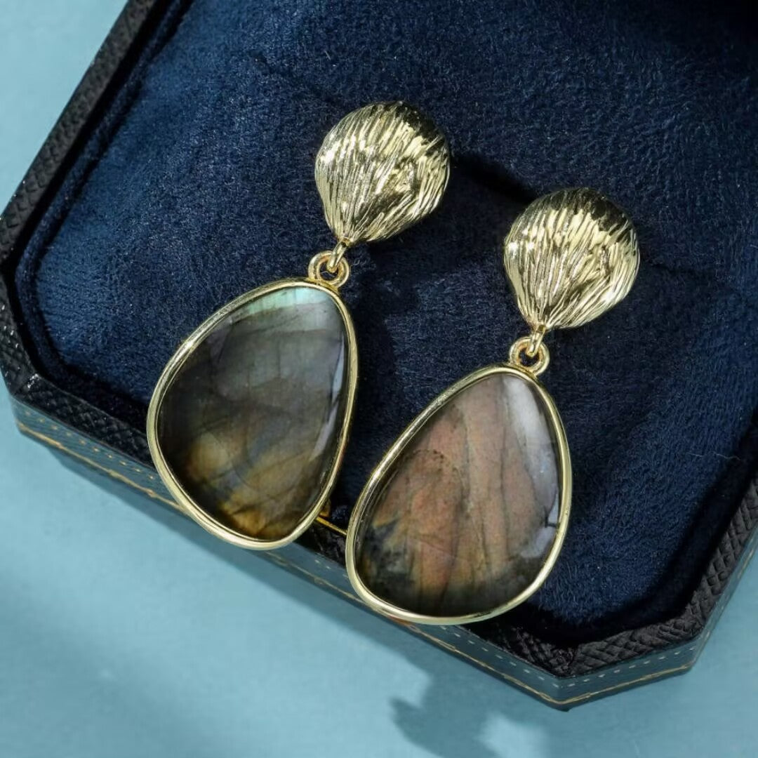 Boucles d'oreilles pendantes avec une pierre de labradorite aux reflets chatoyants, sertie dans un entourage doré, et un fermoir texturé en forme de sphère.