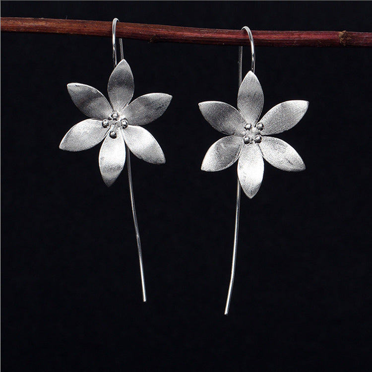 Boucles d'oreilles pendantes en forme de fleur de lotus éclose, en argent, avec une tige fine et des petites perles au centre de la fleur.