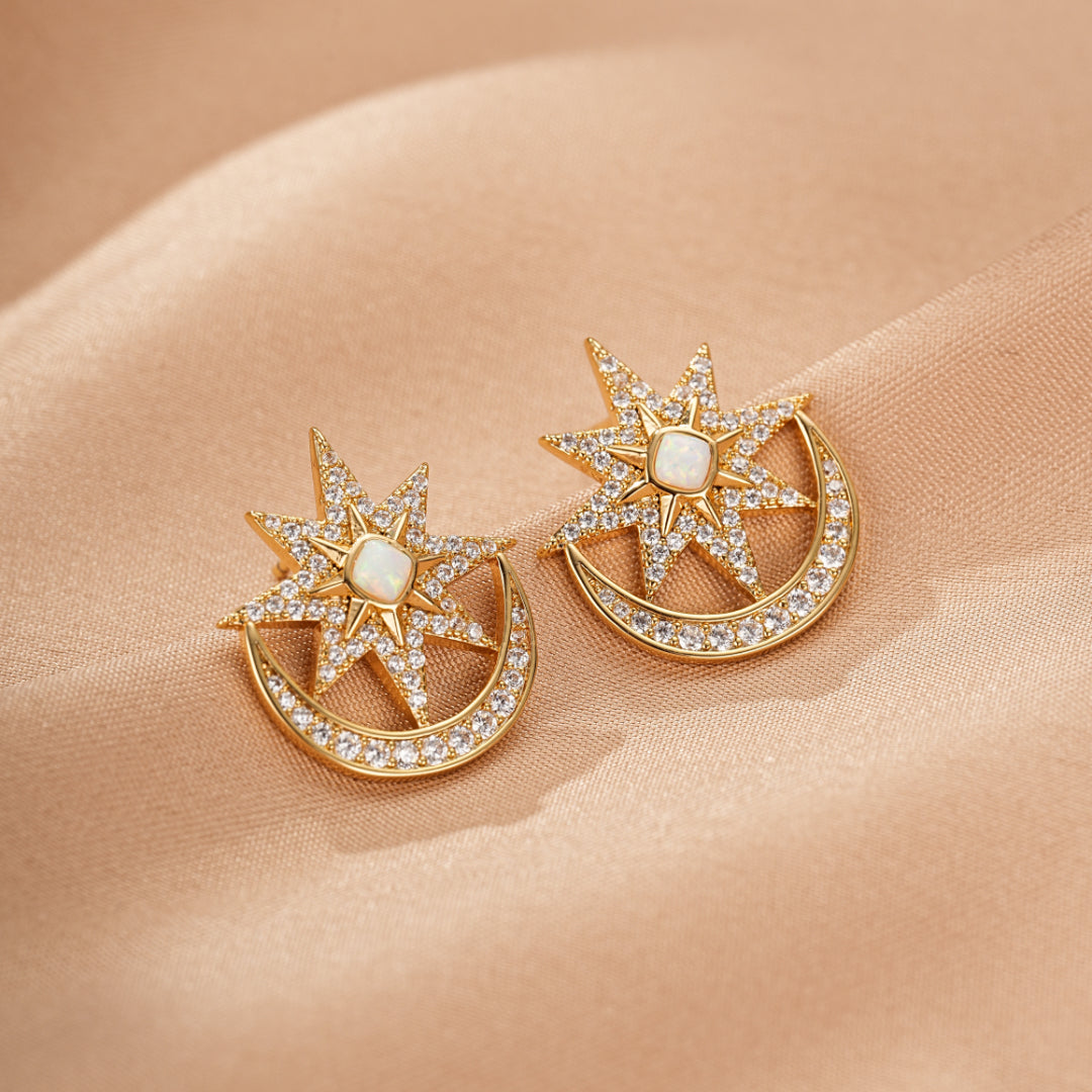 Paire de boucles d'oreilles dorées en forme de lune et d'étoile serties de petites pierres scintillantes et d'une opale centrale.
