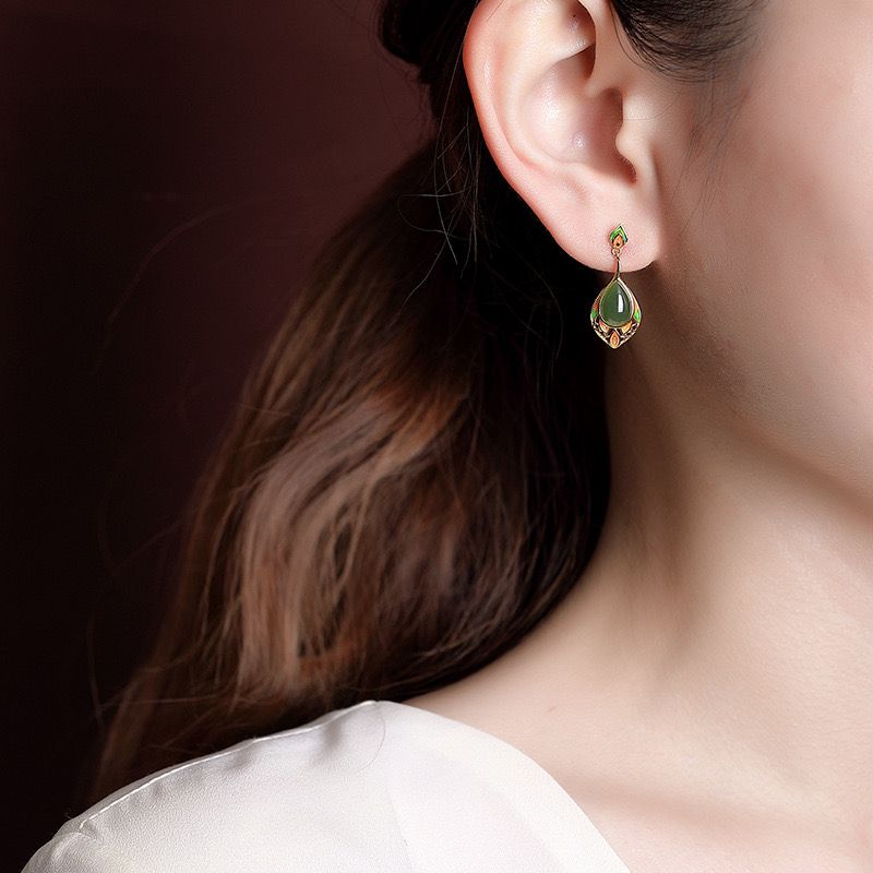 Boucles d'oreilles pendantes en jade vert en forme de goutte, ornées de détails dorés, portées à l'oreille d'une femme.