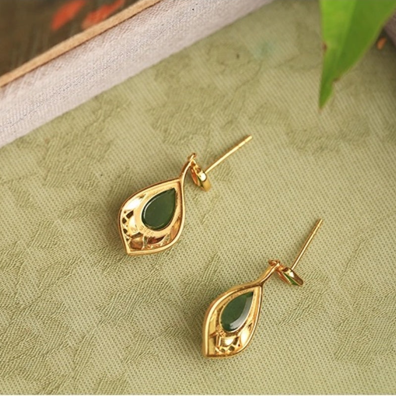 Paire de boucles d'oreilles pendantes en argent plaqué or ornées d'une pierre de jade verte en forme de goutte, sur un fond texturé vert clair.