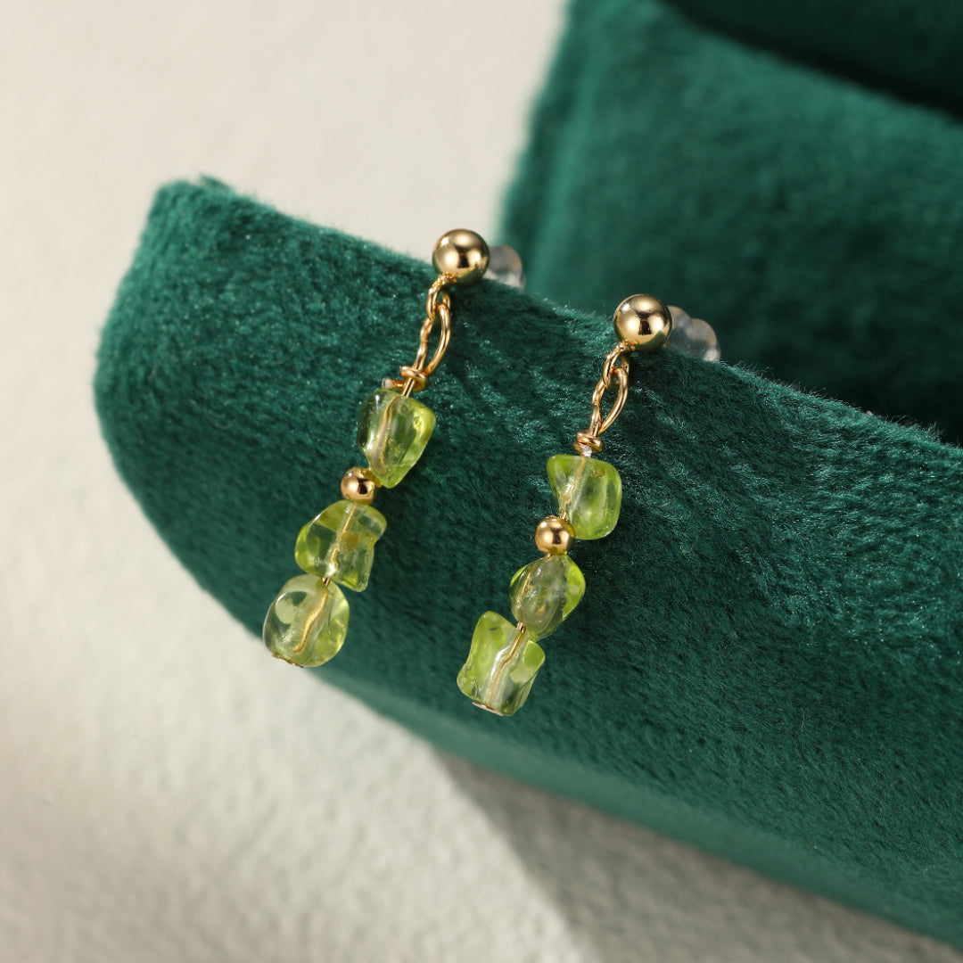 Paire de boucles d'oreilles pendantes en argent plaqué or ornées de trois pierres naturelles de péridot taillées en forme de gouttes, disposées en cascade sur une chaîne délicate.